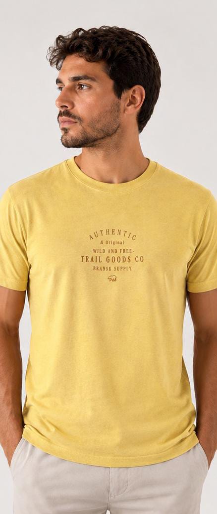 Homem vestindo camiseta amarela estonada Bransk com estampa Authentic Trail Goods Co no peito
